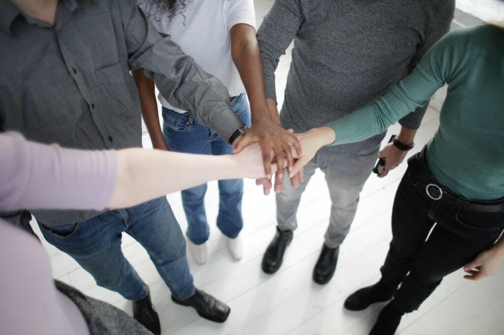 Picture of a group of people all putting arms together. This signifies my call to action of joining me on this endeavor